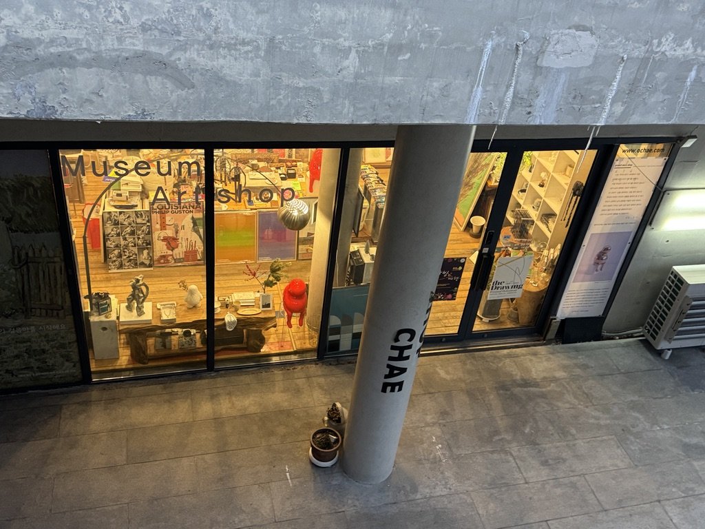 위에서 내려다본 오채 외관. 기둥 뒤 유리창 너머로 따뜻한 조명의 매장과 작품들이 보인다.